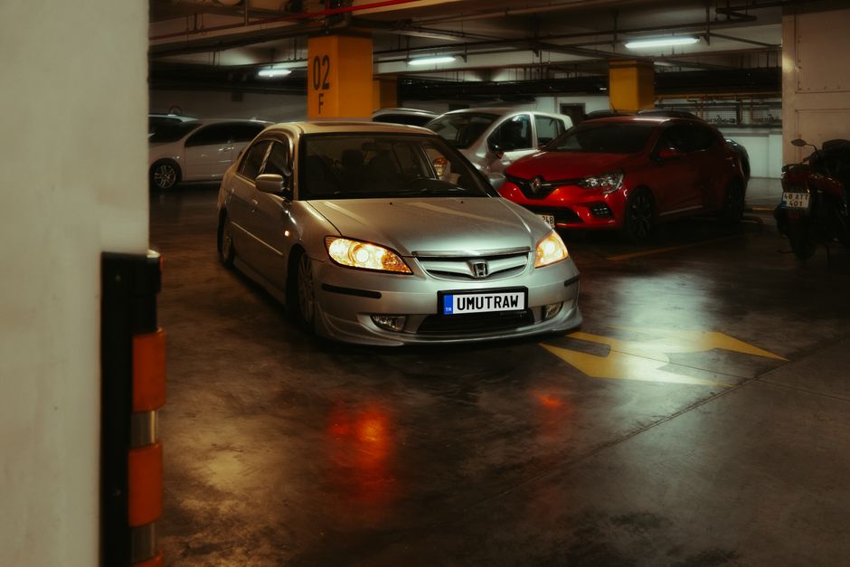 A modern silver car parked indoors with headlights on in an urban setting.